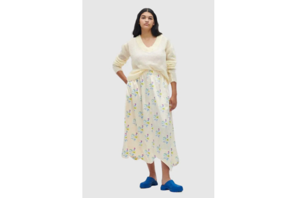 Woman in cream jumper, floral skirt and blue clogs