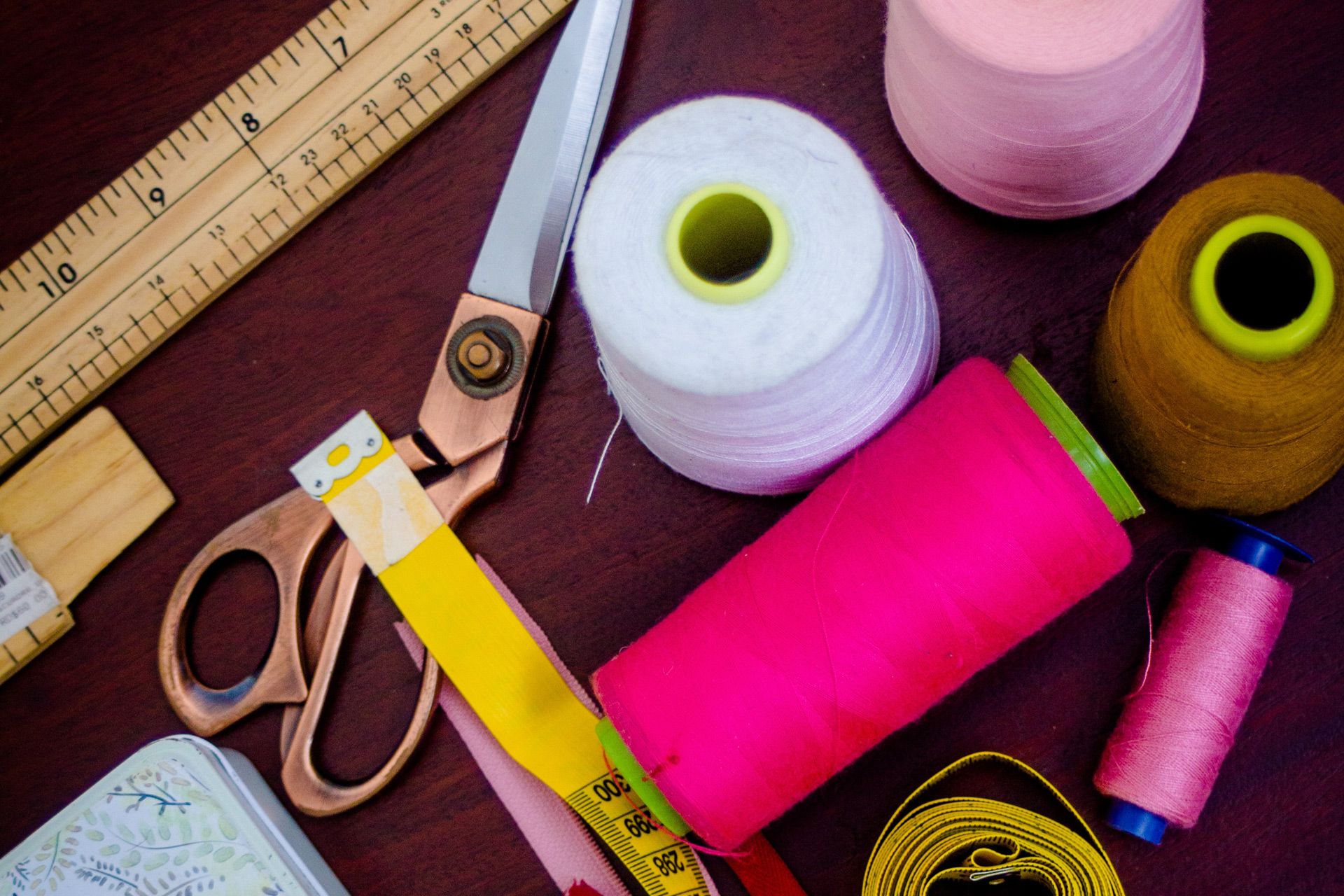 Sewing table featuring scissors, spools of pink and white thread, rulers and a tape measure.