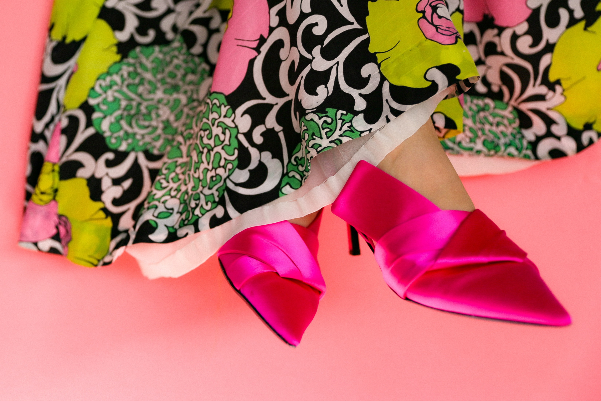 Feet in pink heels peeking out of patterned long skirt