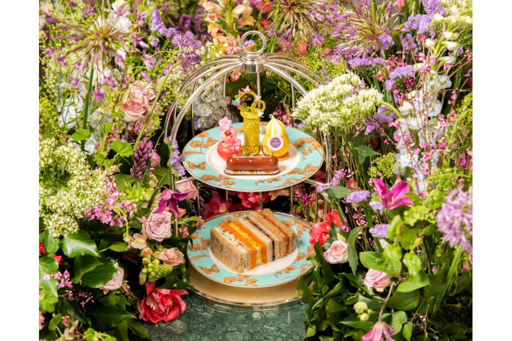 Afternoon tea stand with cakes, scones and sandwiches sat in vines and flowers