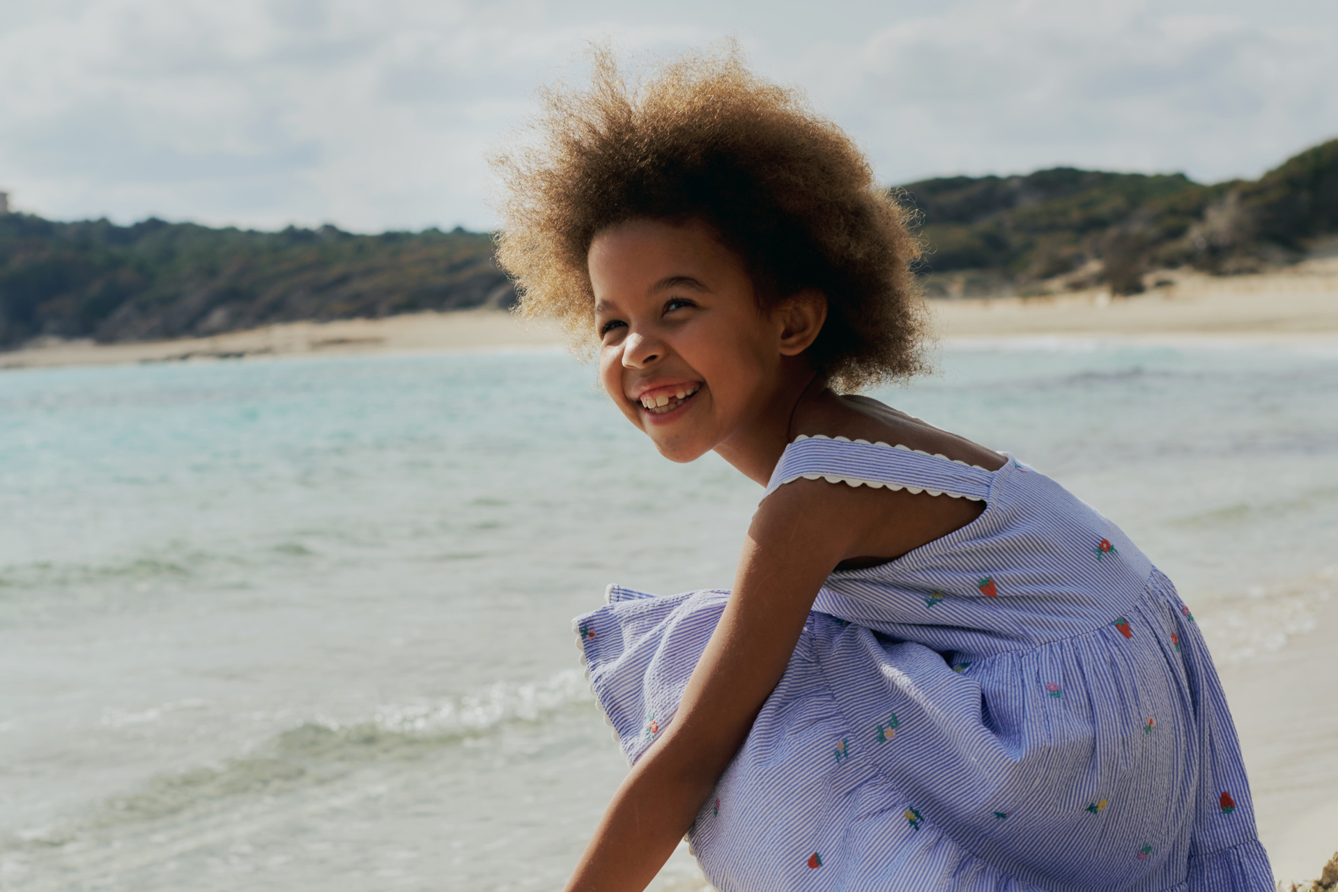 Young girl crouched down in a summer dress at the beach