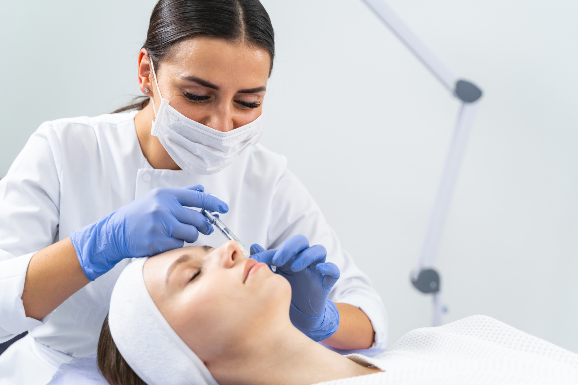 Dermatologist injecting a cheek filler to a young patient lying with her eyes closed during the anti-wrinkle injection in a beauty salon | aesthetic doctors