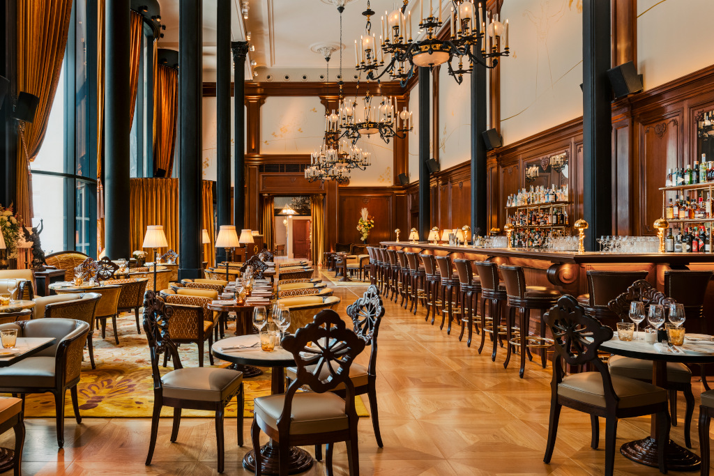 grand parisian cafe with double height ceiling and tables and chairs with wood panelled walls and black columns