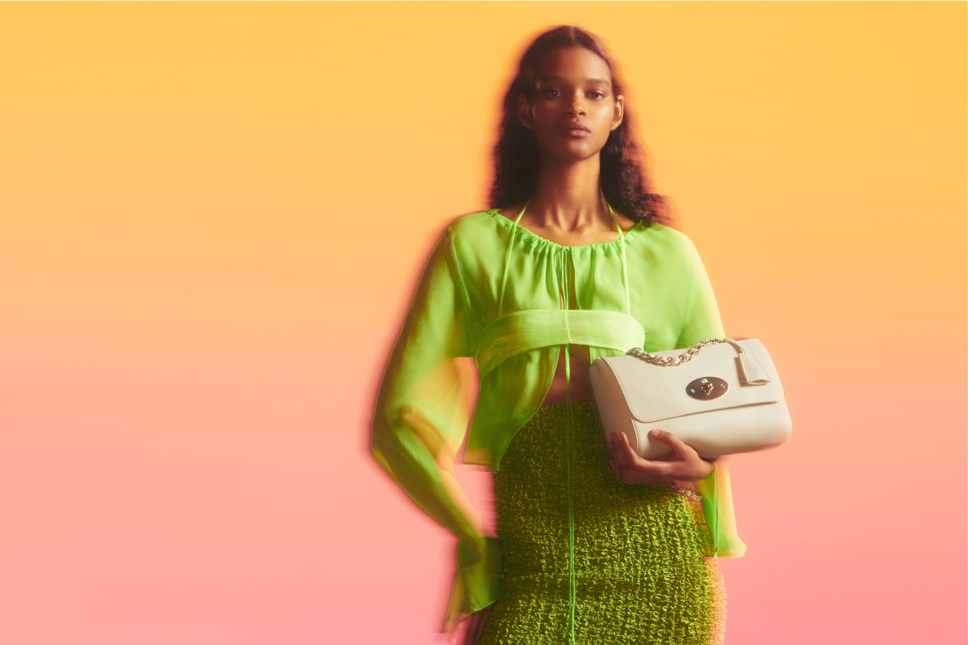 Woman in neon green holding a cream handbag