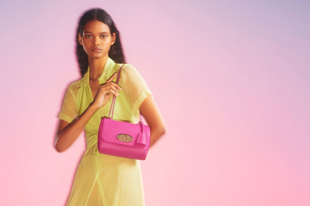 Woman in yellow dress holding pink handbag on light purple background