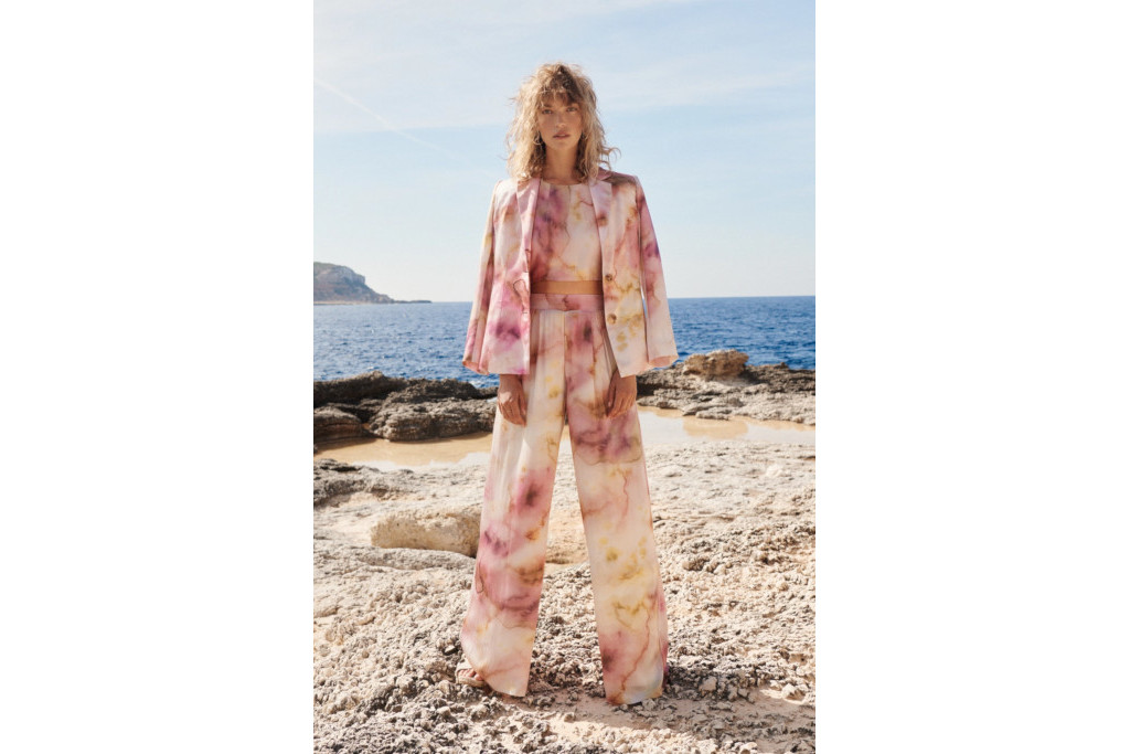 Model in pink patterened suit stood on cliff overlooking sea