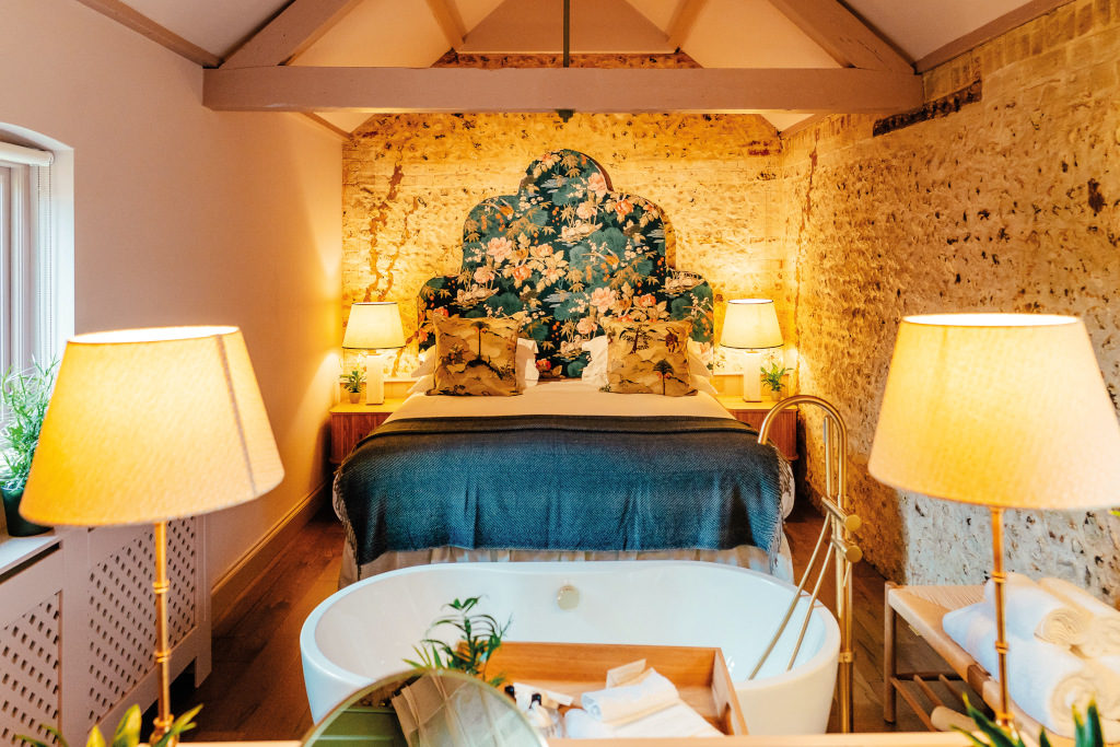 The Grosvenor Hayloft bedroom with brick wall, warm lighting and free standing bath tub