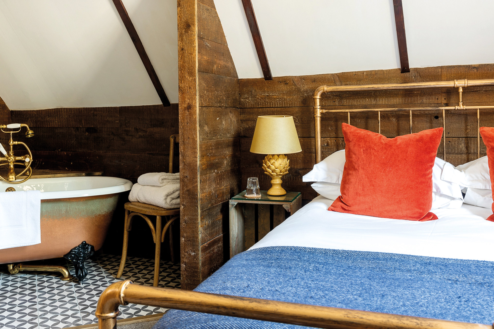 Bedroom at Tudor Farmhouse Hotel with a copper freestanding bath and blue and red accents.