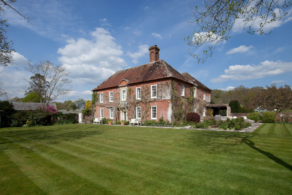 red brick wisteria clad english country house with white pane windows, sitting in front of garden exterior shot from side
