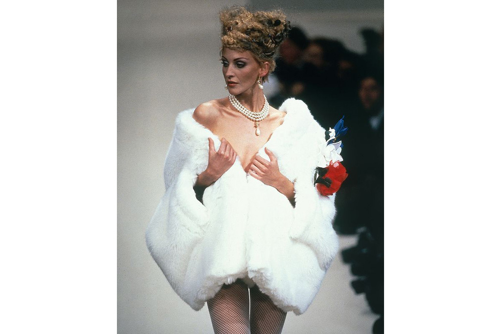 Model in white fur coat and pearls walking down runway