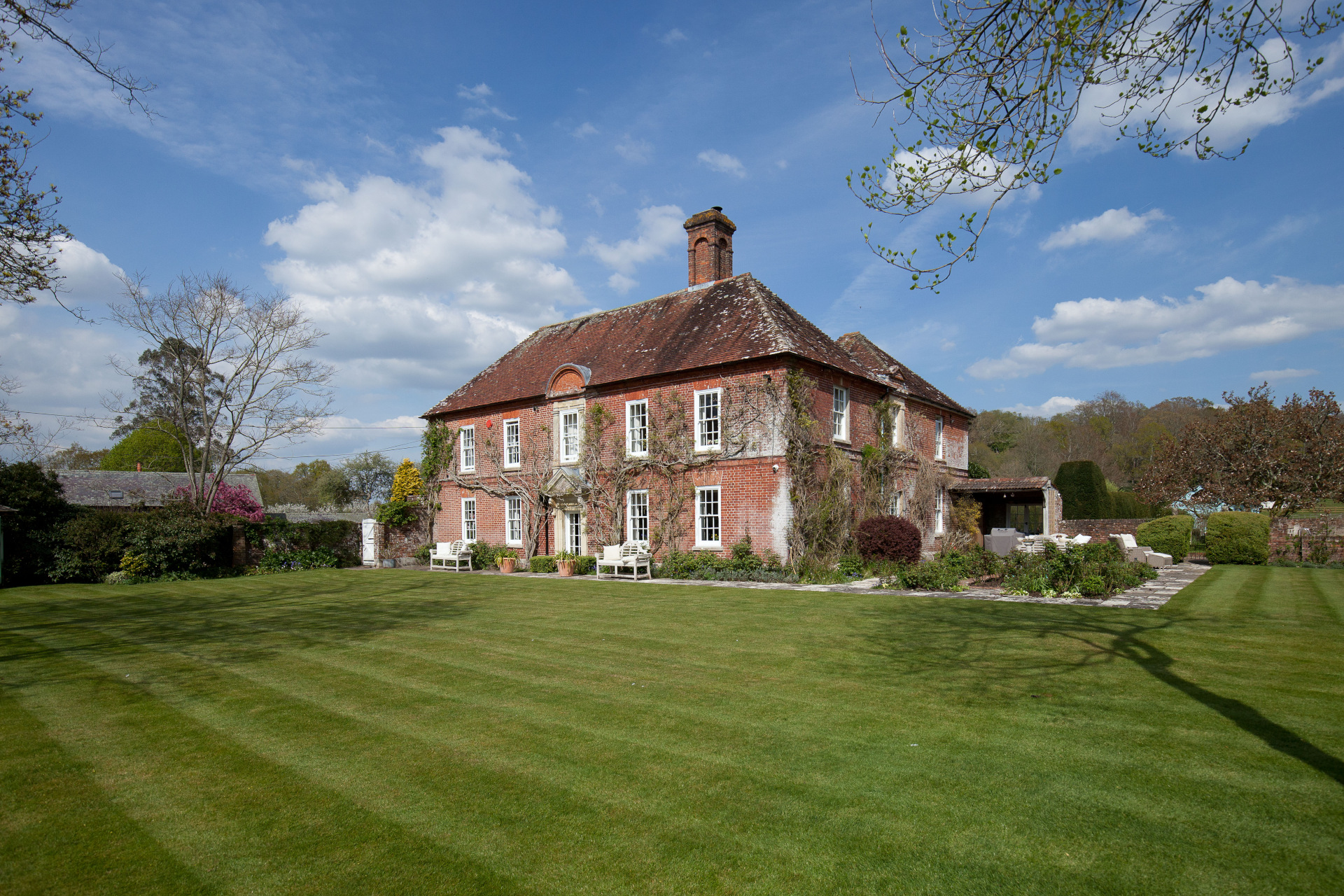 red brick wisteria clad english country house with white pane windows, sitting in front of garden exterior shot from side