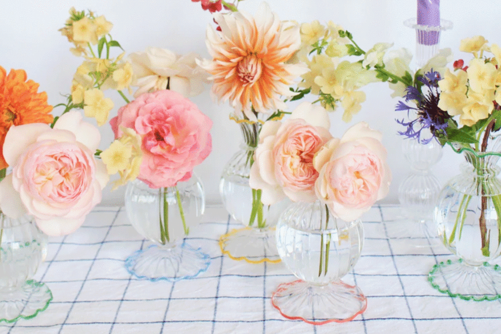 a group of colourful bud vases with flowers on a table by Style Your Spaces
