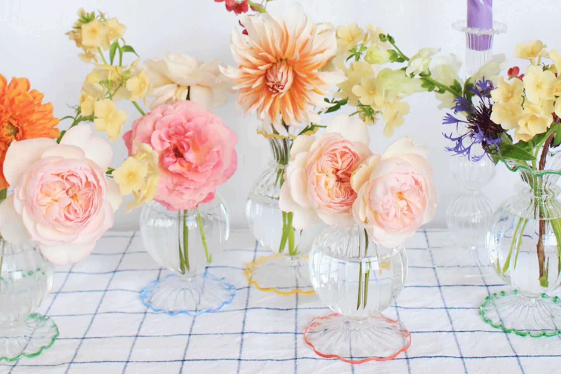 a group of colourful bud vases with flowers on a table by Style Your Spaces