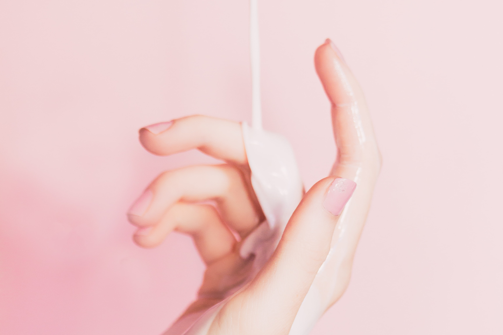 Cosmetic cream dripping on hand, with pink brackground
