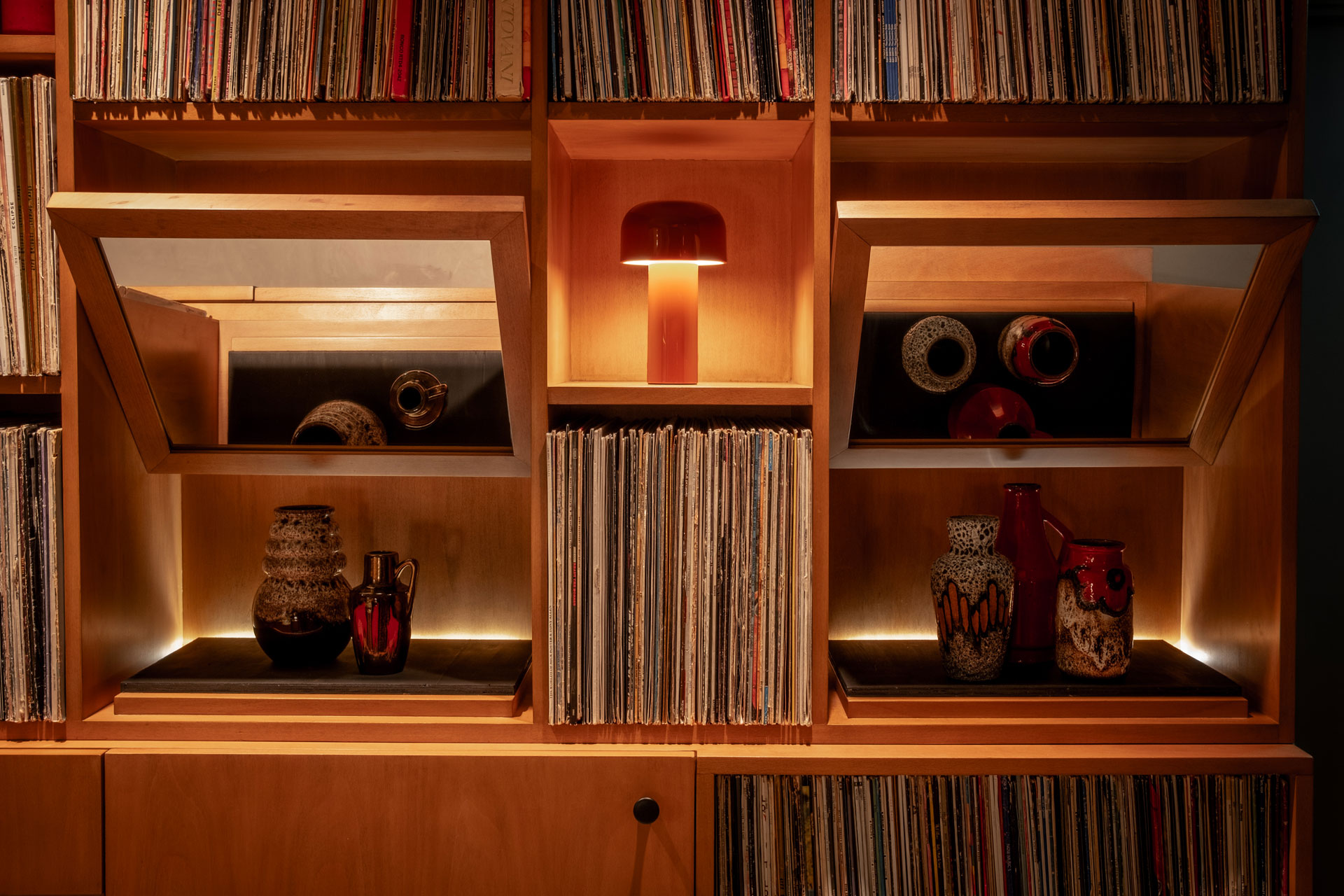 View of the interiors of the bar at Seed Library, which has stacks of Vinyl records and lowly lit lamps amongst wood shelving