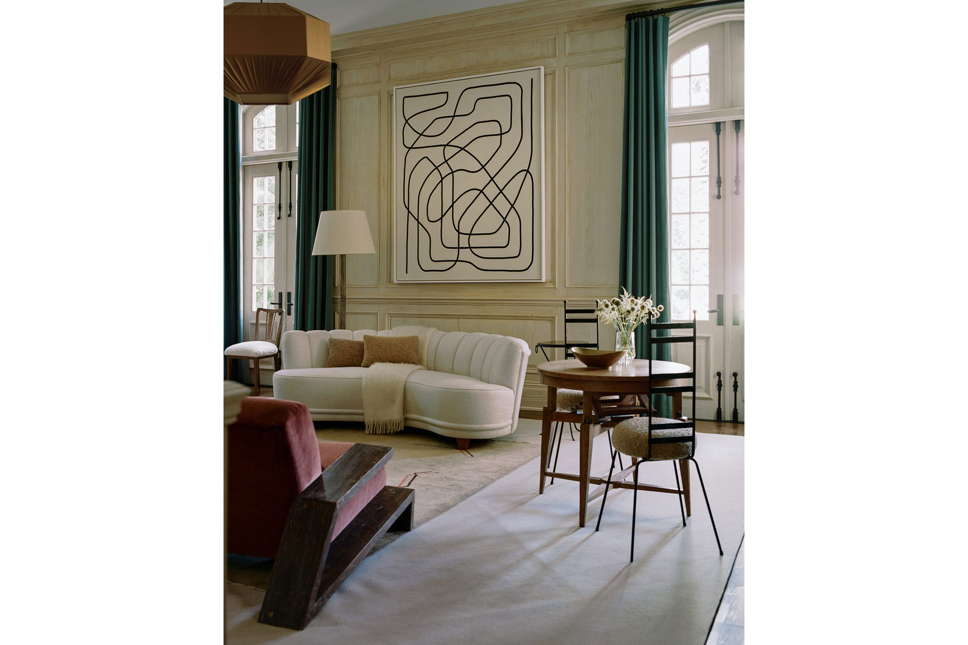 a living room with an abstract linear painting, cream sofa, and two tables and a chair