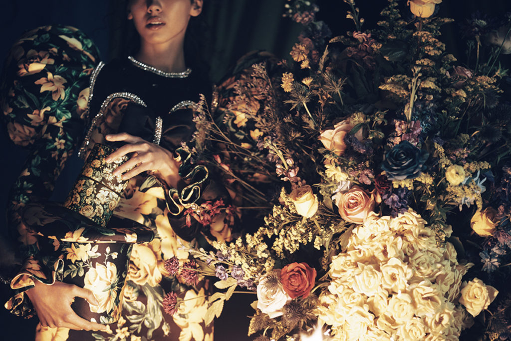 Close up of models in floral print clothing holding boxes of candles