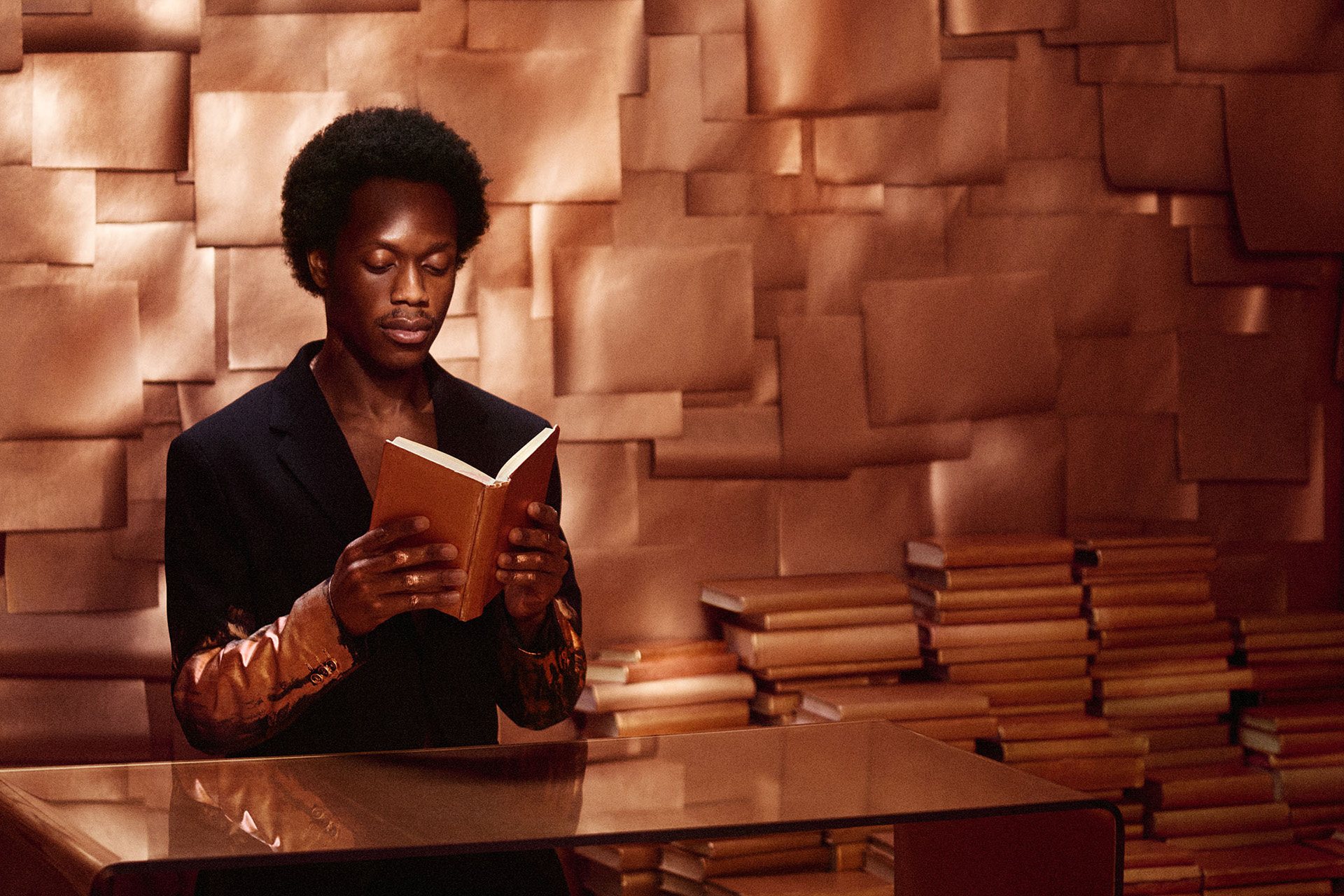 A Black man reading a book in a bronze room