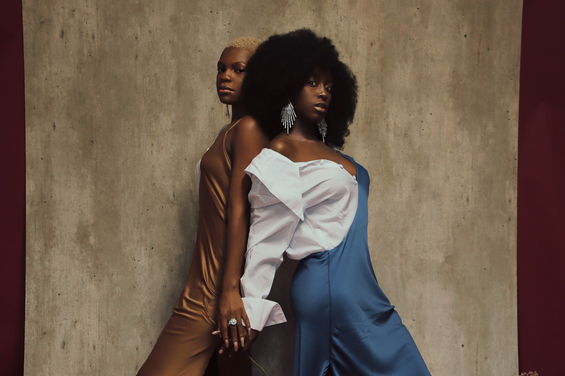 Two black models in formal dress stood back to back holding hands - hair trends 2024