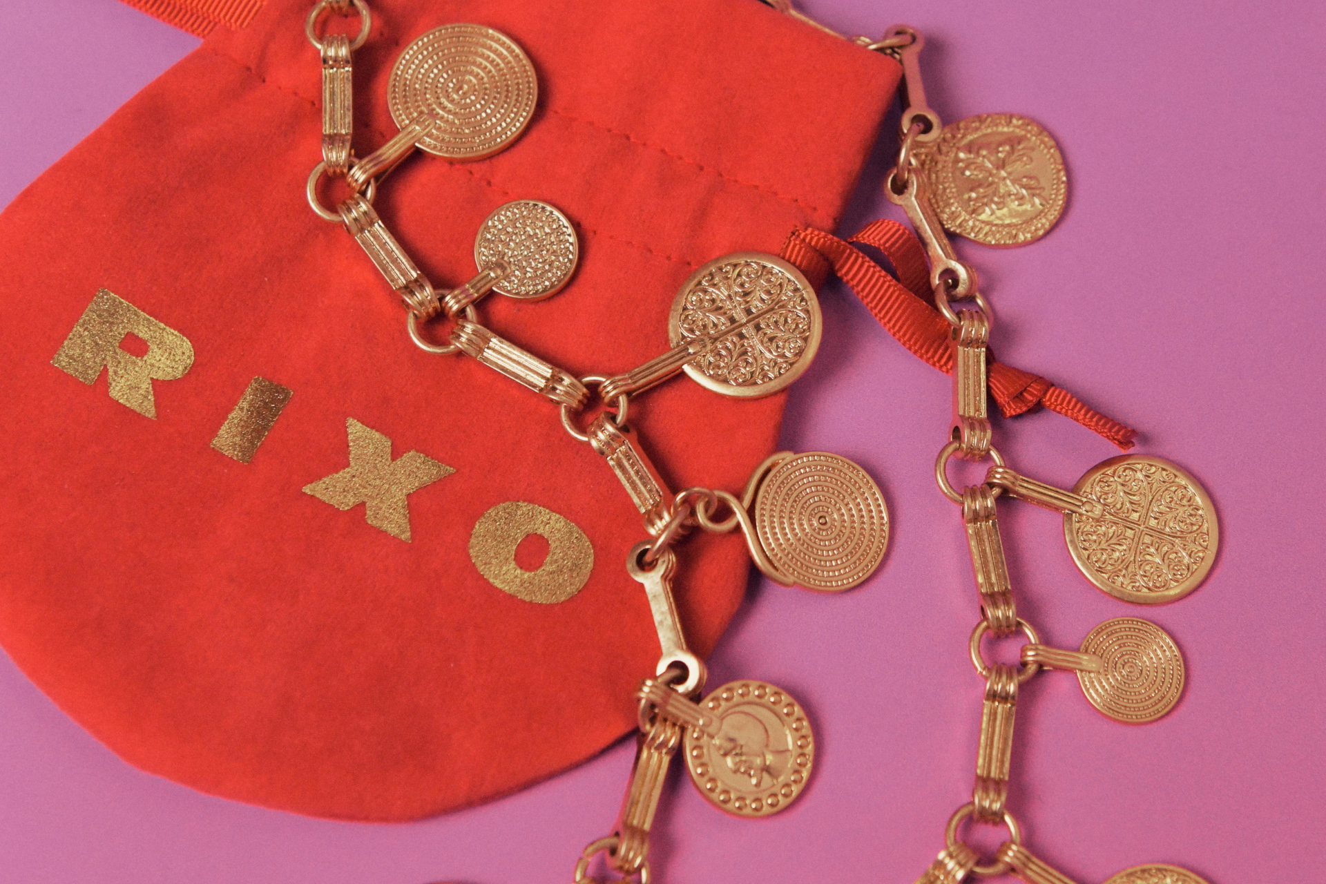 Red pouch with 'RIXO' spelt on the front in gold, with a gold necklace on top
