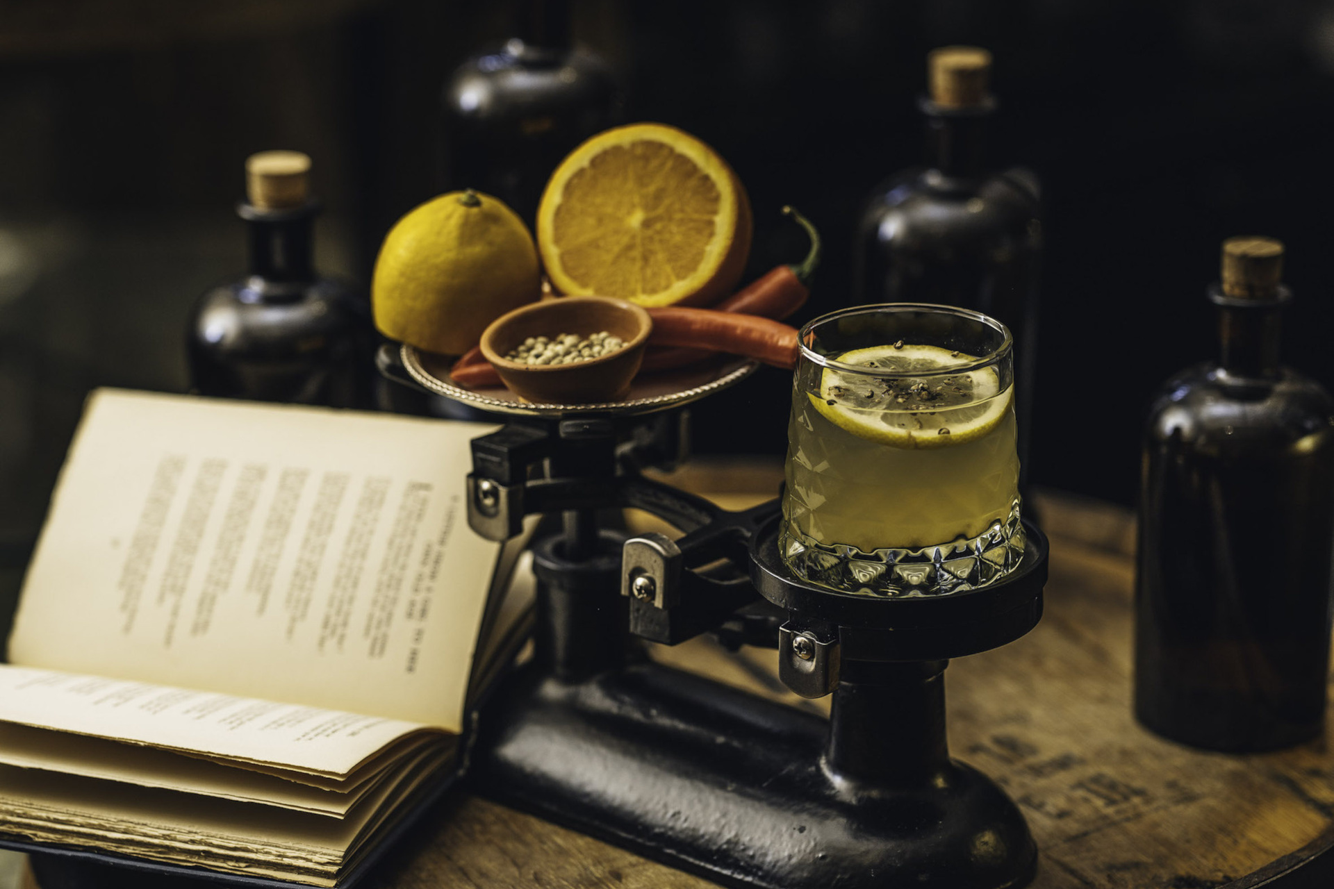 Cocktail and fruit resting on old fashioned scales on table, next to open book