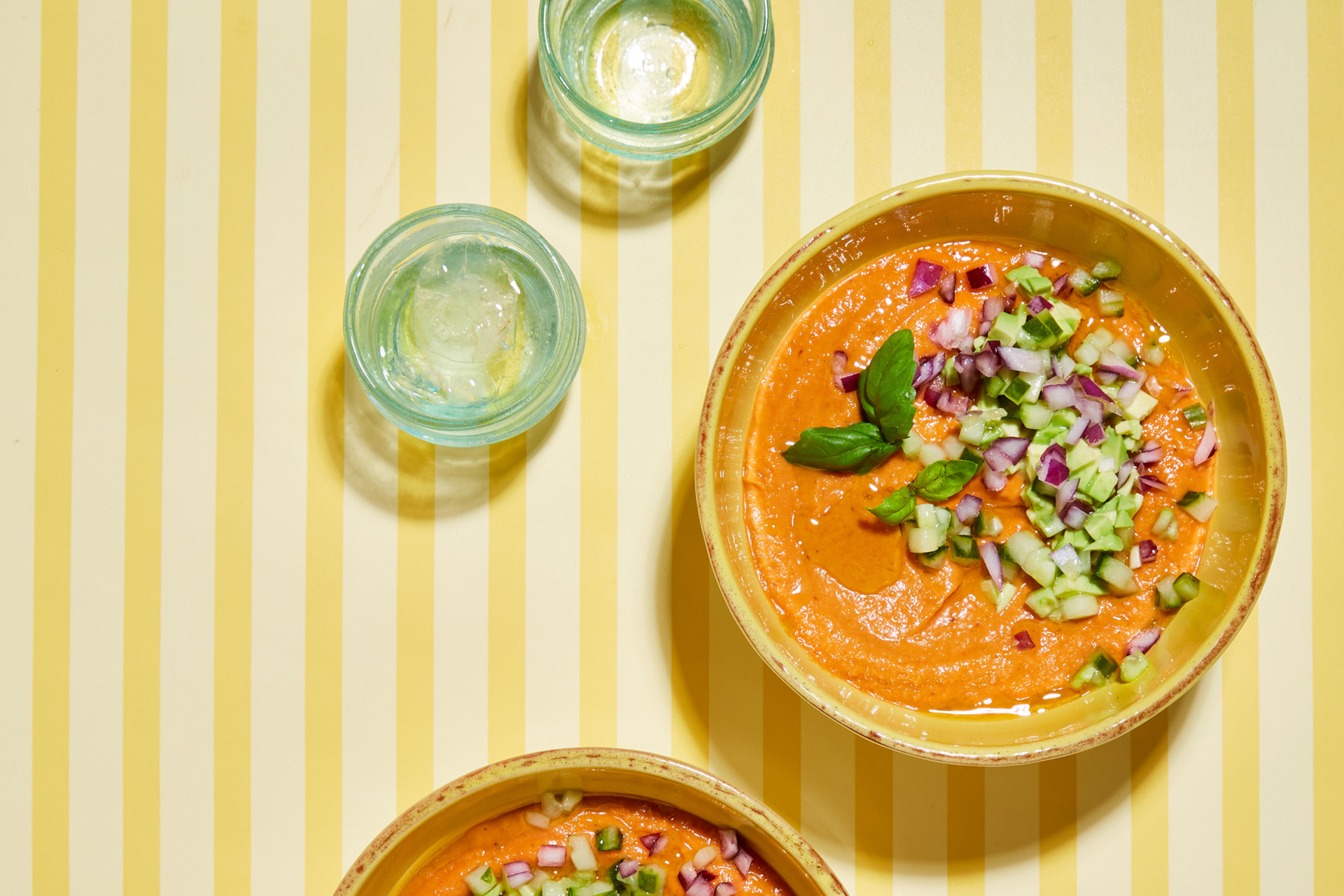 Salmorejo in bowls set on yellow striped table next to glasses of water