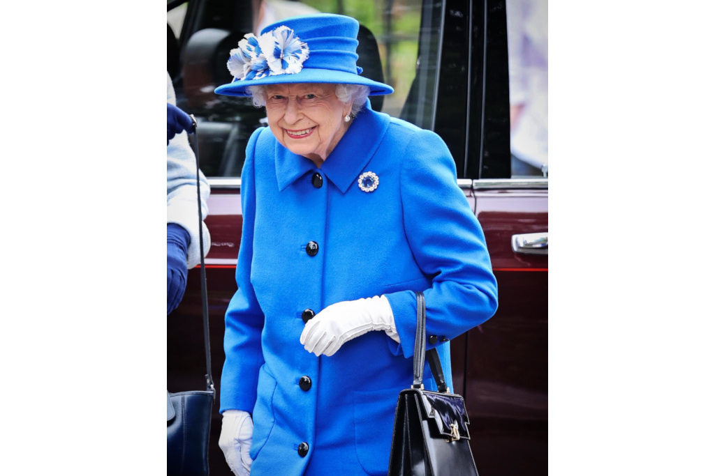 The Queen in a blue coat and hat, white glove and a black handbag