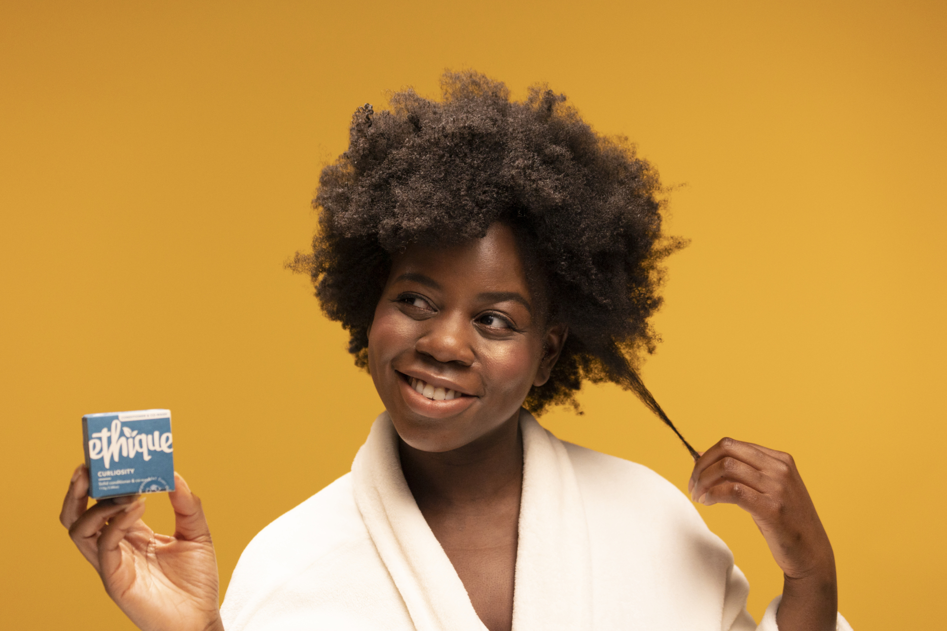 Model with afro hair holding a shampoo bar, on orange background