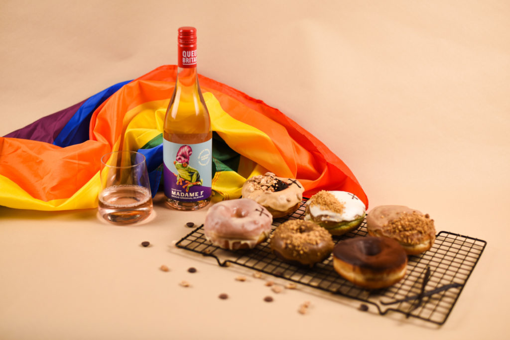 A tray of doughnuts next to a bottle of wine and a rainbow flag
