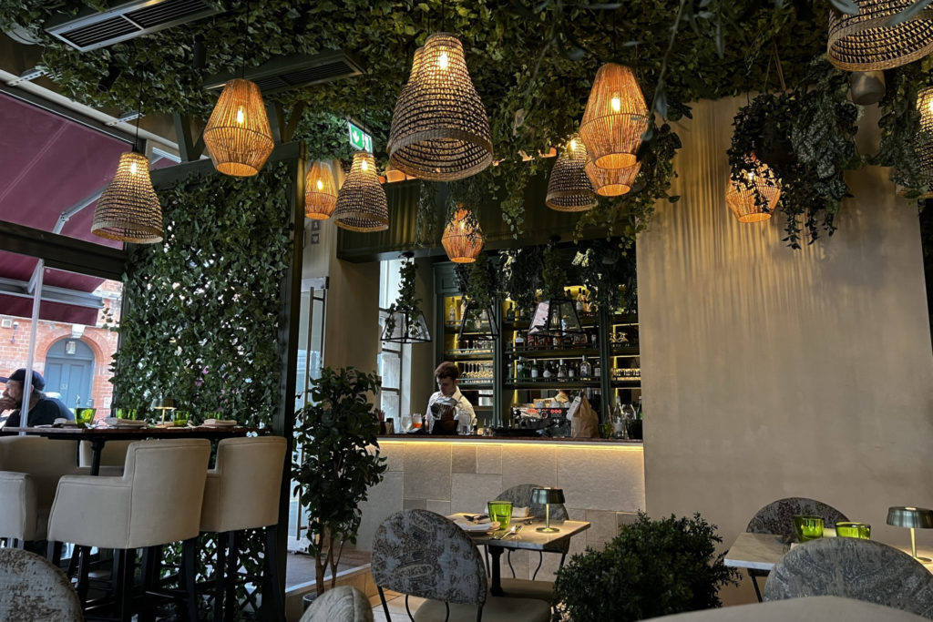 Interior of Italian restaurant Como Garden, showing the bar and the leafe-covered walls and ceiling, with warm hanging lights overhead