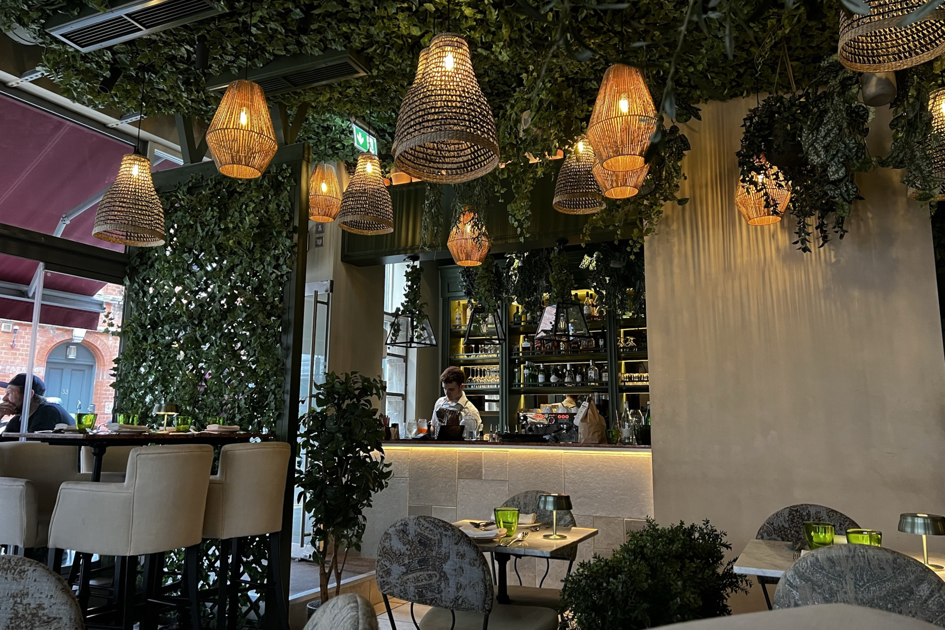 Interior of Italian restaurant Como Garden, showing the bar and the leafe-covered walls and ceiling, with warm hanging lights overhead