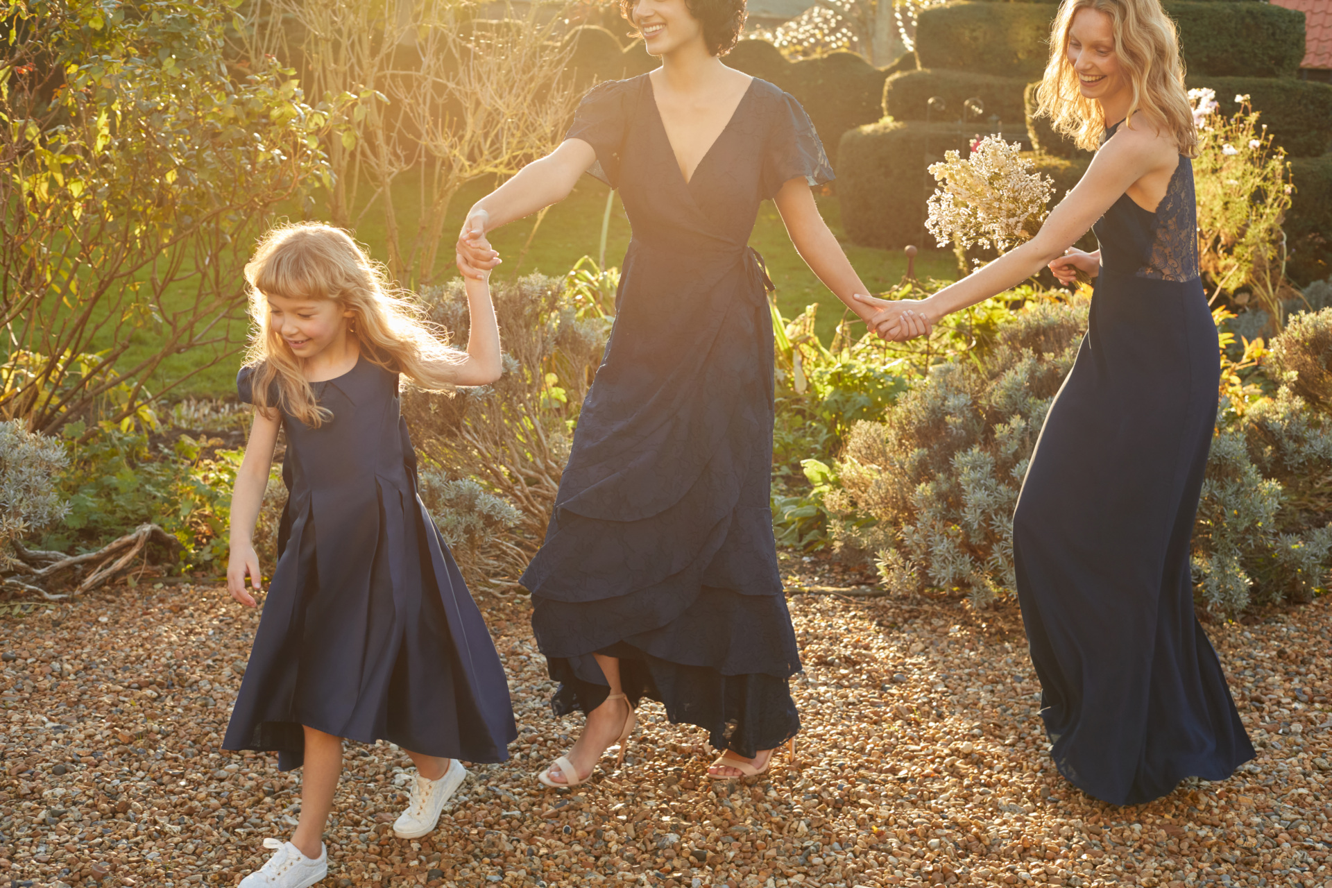 Bridesmaids and flower girl all holding hands at sunset