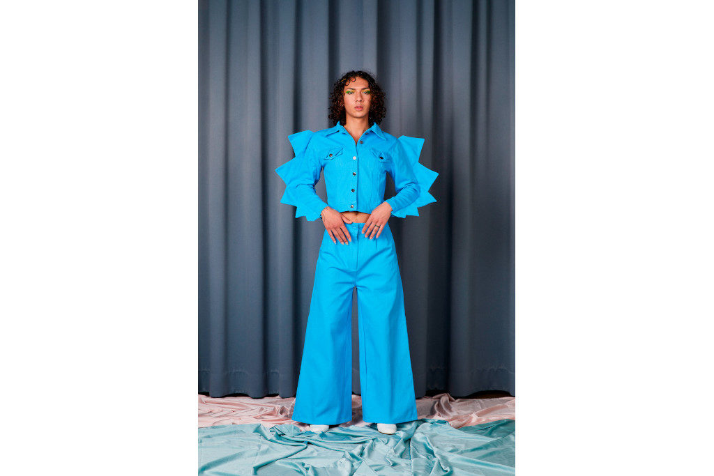 Model in blue denim co-ord with spikes on the arms, stood in front of grey curtain