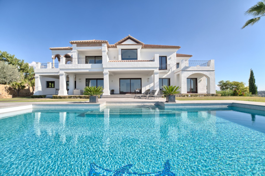 Sunny view of a white villa with a large blue pool