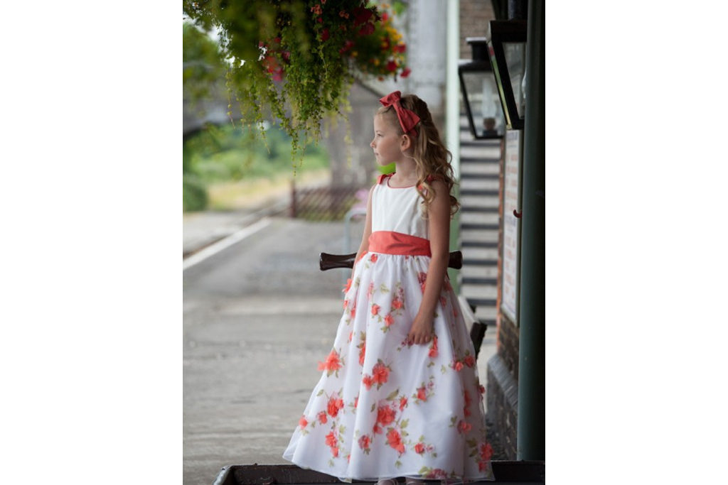 Girl stood in white dress with coral flowers and sash