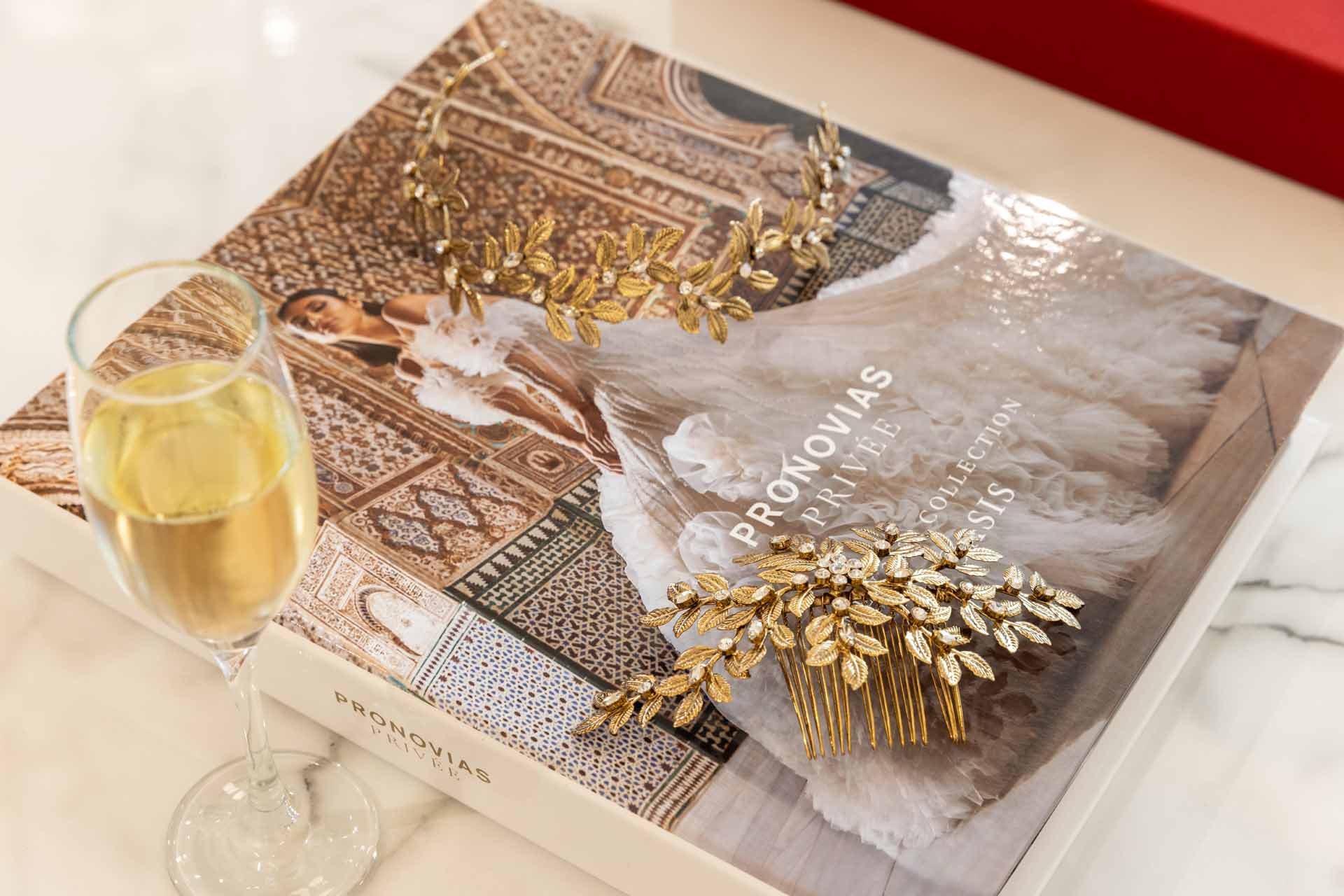 Close up of Pronovias lookbook, gold hairclip and glass of champagne on marble table
