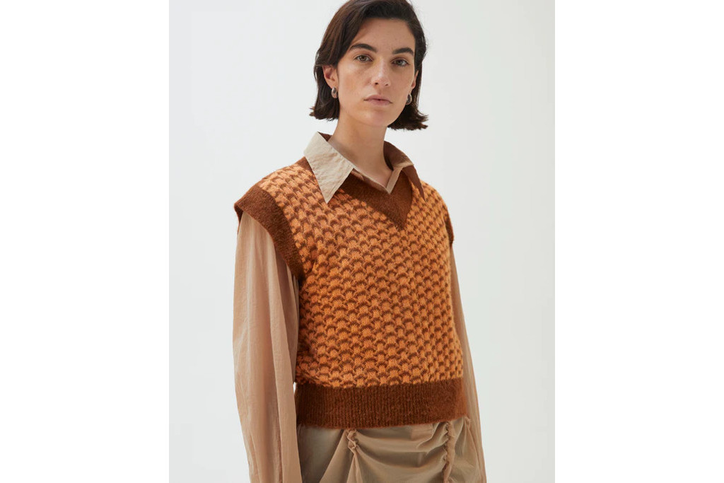 Model in prange and brown sweater vest and neutral shirt