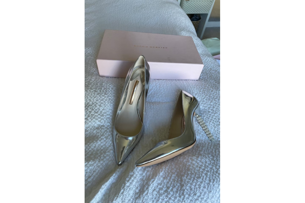 A pair of silver heels set in front on pink shoe box on a bed