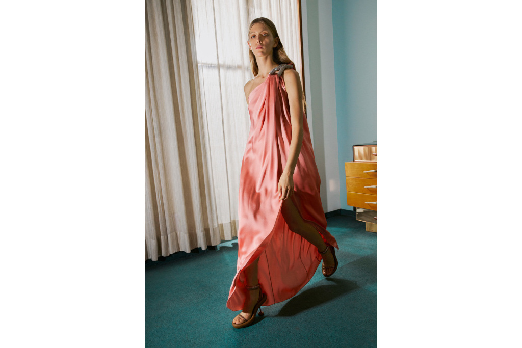 Model walking through room in long pink satin gown with one shoulder