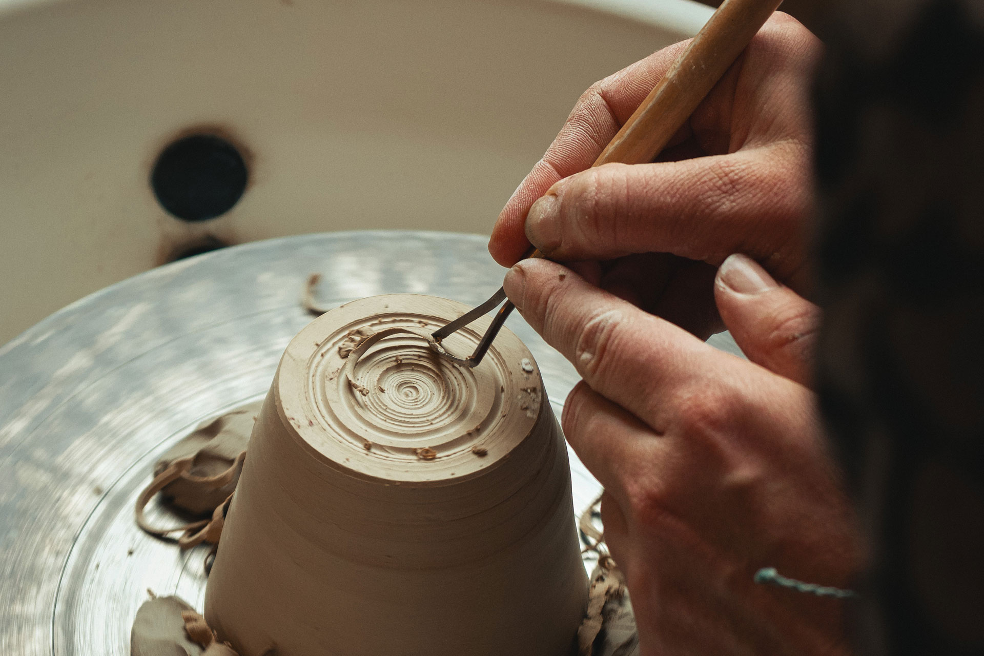 hands carve out a pot on a wheel during a pottery class