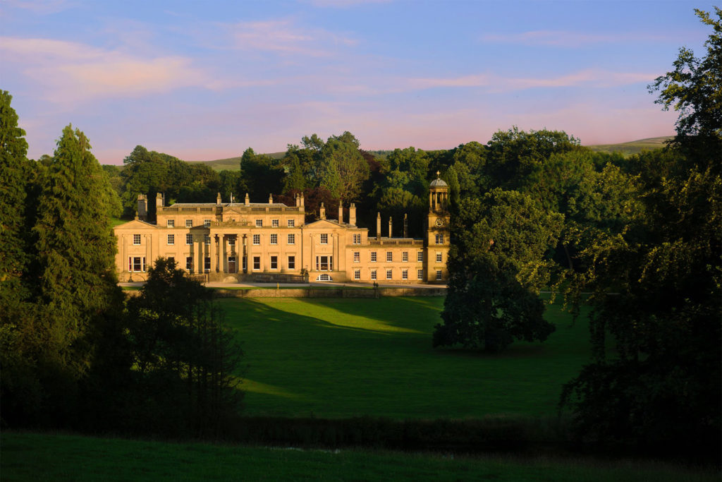 exterior shot of Broughton Hall amongst woodland and grounds in early evening with sun glowing golden on the building