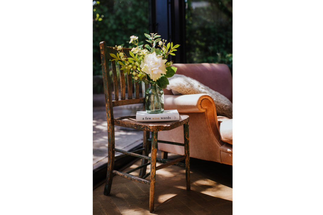 a fake bouquet of flowers in a vase on a wooden chair outside, by Hoax 