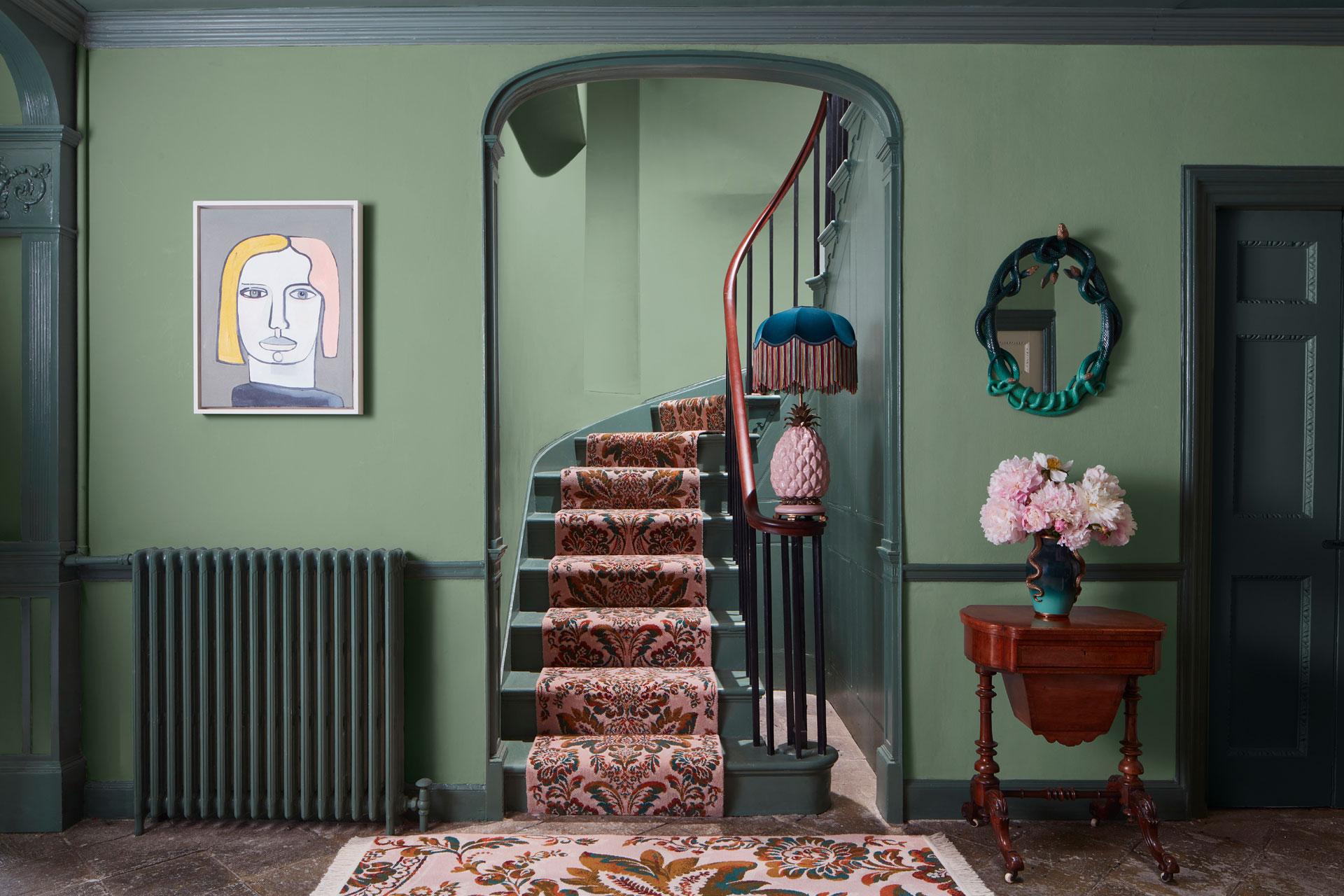 A view of a carpeted stair case with green walls either side, painted in Jadeite green by House of Hackney