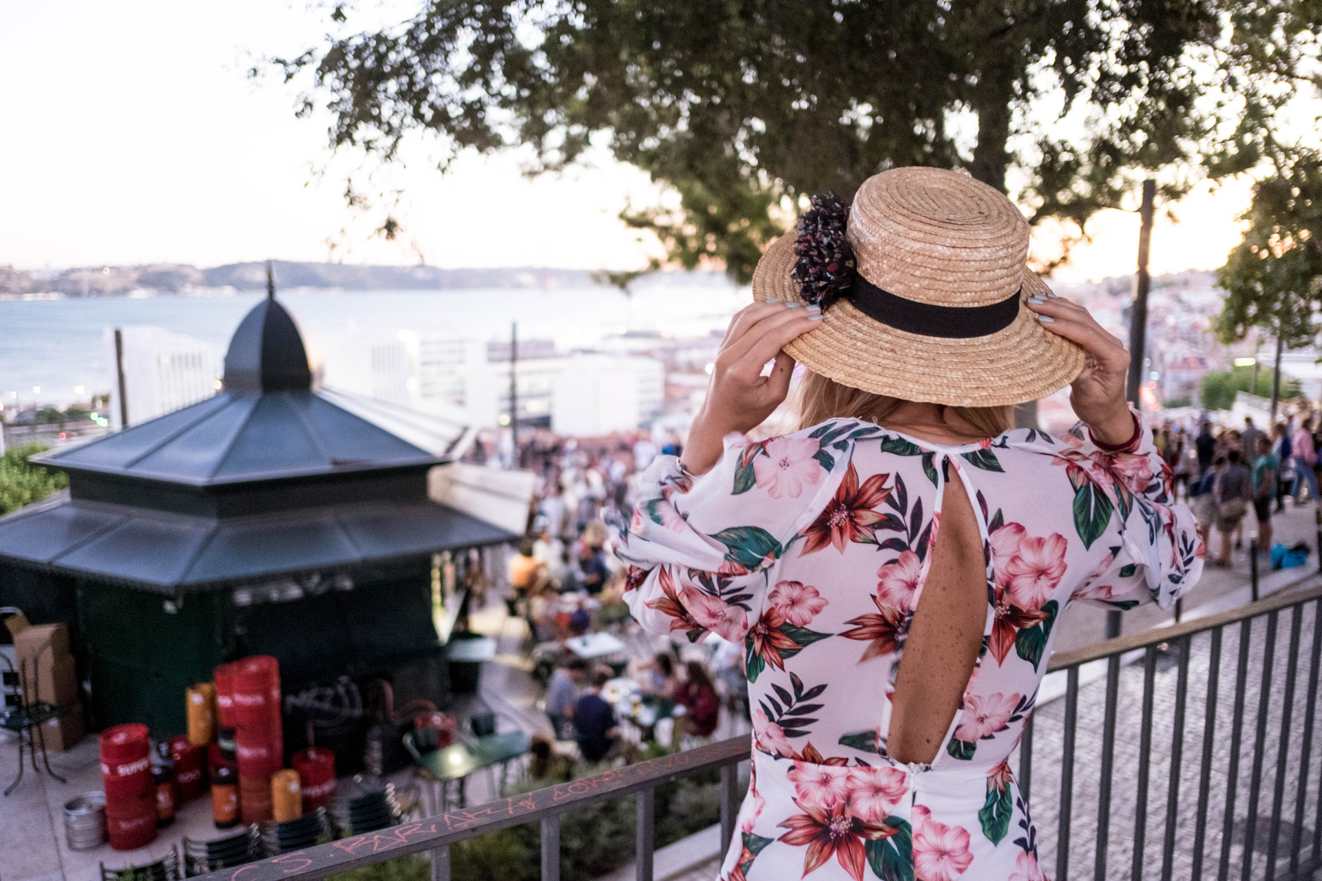 Woman in summer dress and hat overlooking busy street by the water