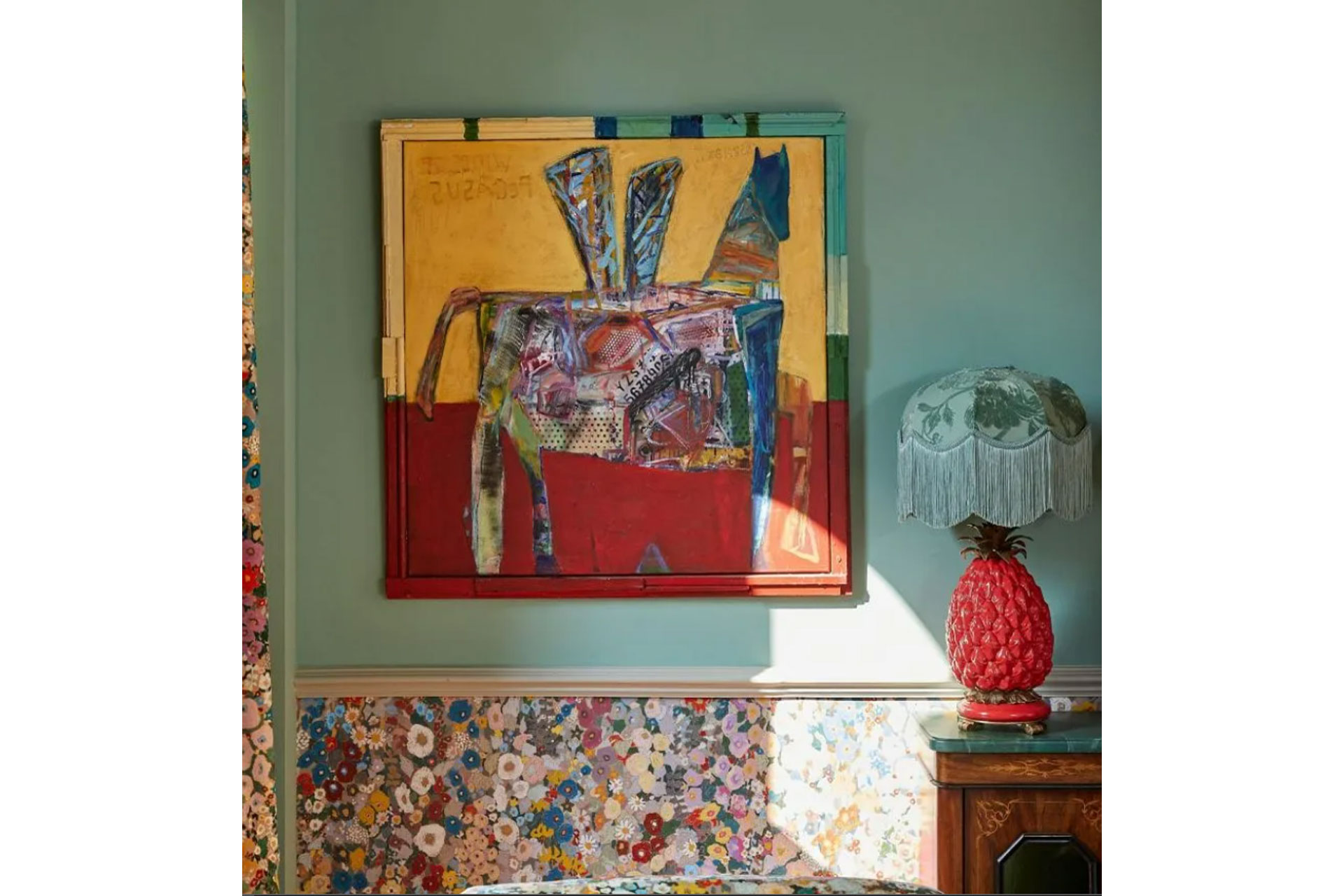 a yellow abstract painting hangs amongst a light green wall and a over the top red lamp in a maximalist interior style