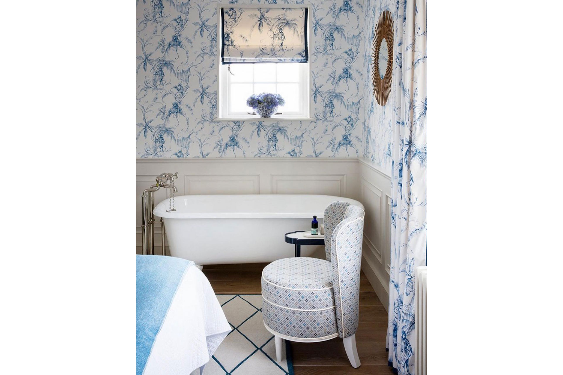 a bathroom interior with blue floral wallpaper and a blue armchair that's designed by Nina Campbell