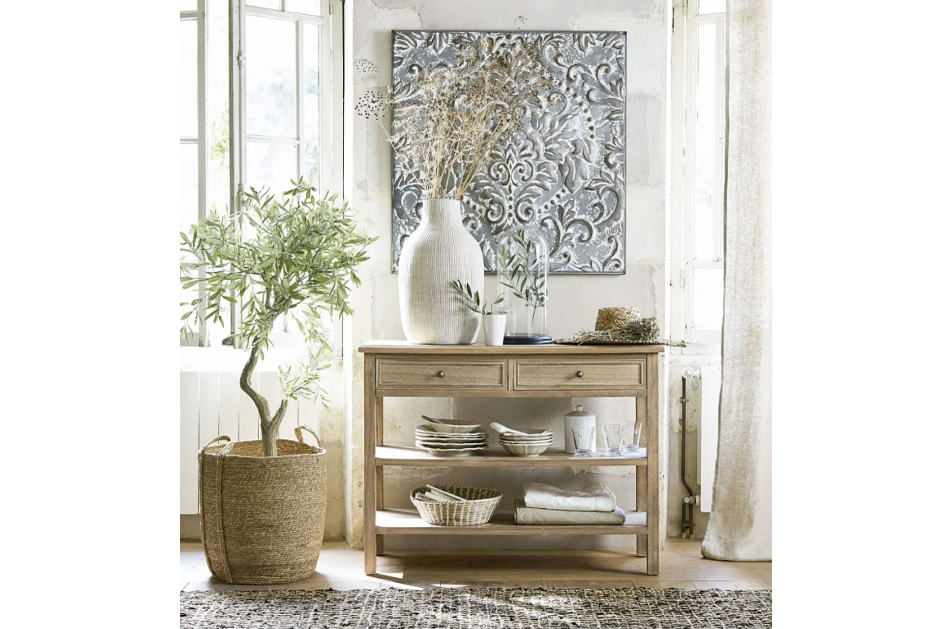 A fake olive tree sits in a light airy living room next to a console table