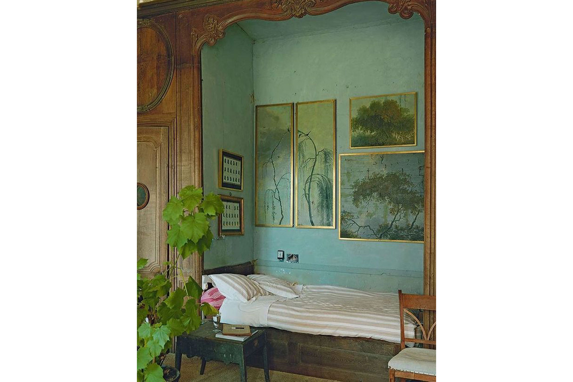a blue walled bedroom with antique paintings and plants