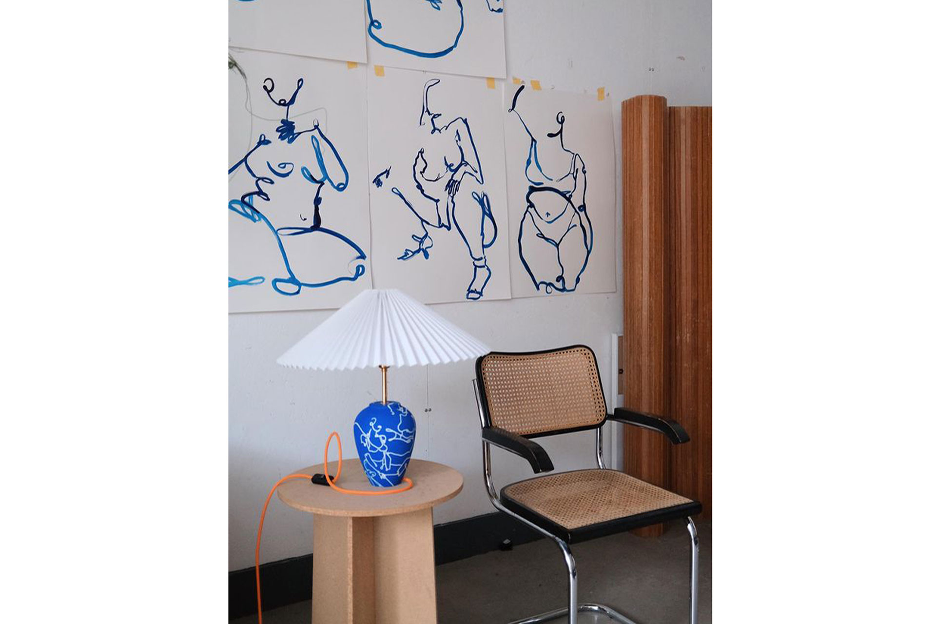 a room with a lamp and blue figurative paintings by Partnership Editions