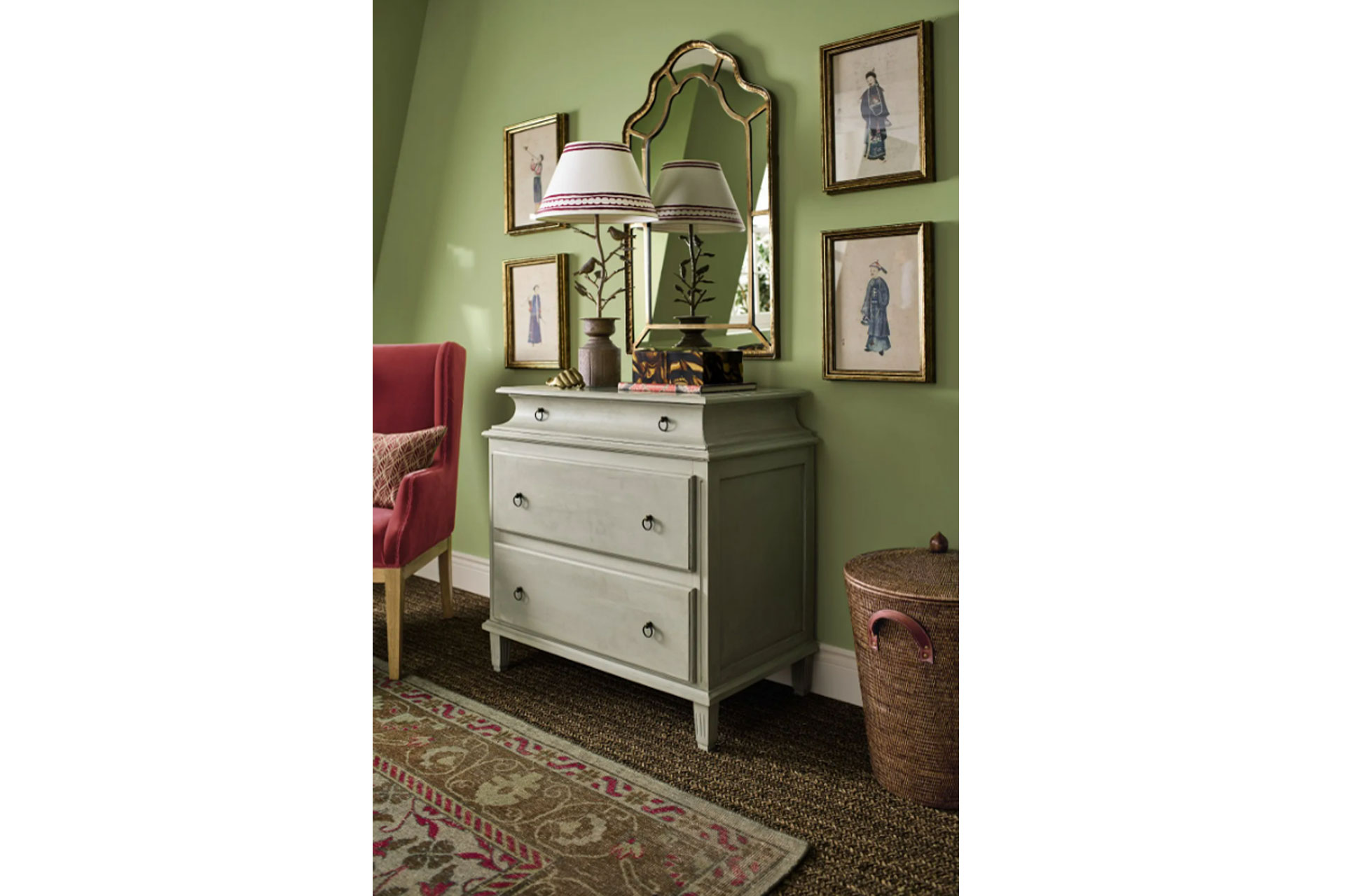 a green dresser stands next to a pea green wall in a bedroom with antique paintings hanging either side